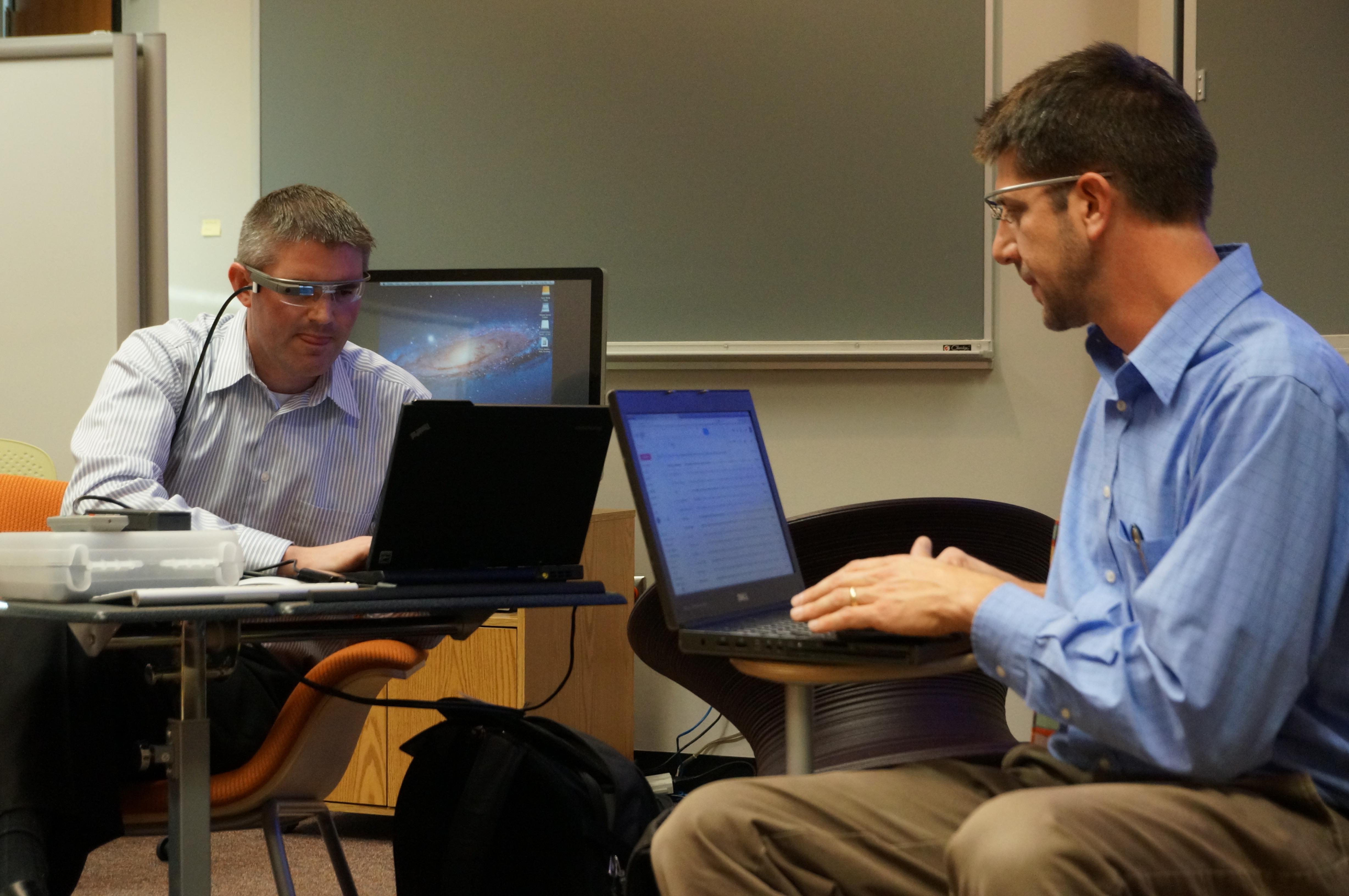 Two men wearing google glass working on their laptops